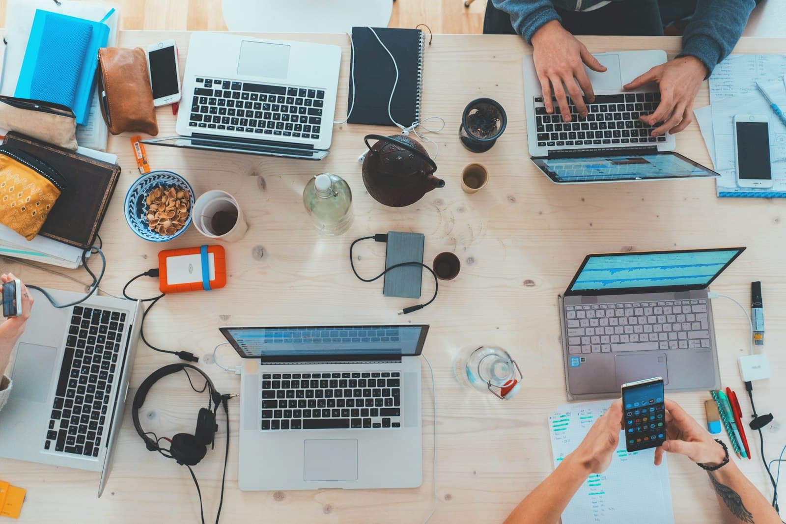 Bureau van bovenaf vol laptops, telefoons en notities, handen aan het werk